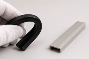 Flexible rubber profile vs rigid plastic channel, hand bending black rubber beside stable plastic extrusion.