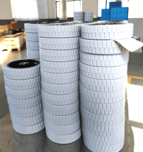 Floor scrubber wheels 200mm, stacked in warehouse, white non-marking tread with ribbed pattern, designed for cleaning machines on smooth floors.