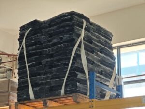 A stack of rubber compound sheets secured with straps on a pallet in a warehouse.