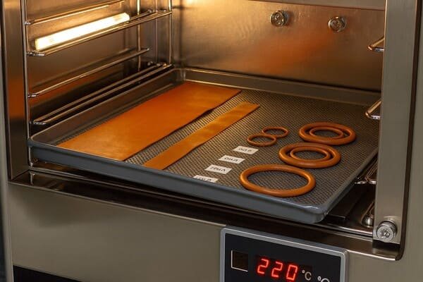 silicone rubber oven aging test, orange sheets and O-rings on metal tray, 220°C heat exposure to evaluate high temperature seal performance.
