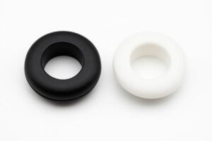 Rubber and plastic grommets, black and white, side-by-side comparison, illustrate material differences for cable protection in electrical panels.