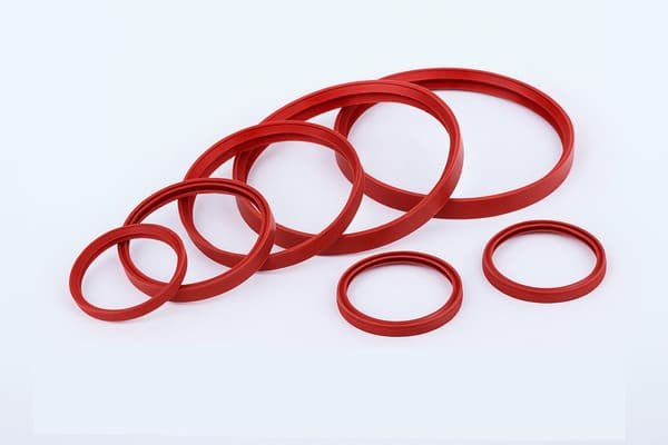 Red rubber sealing gaskets, multiple sizes, arranged in a semi-circle on a white background, showing silicone gaskets for industrial pipe or valve sealing, high-temperature resistant.