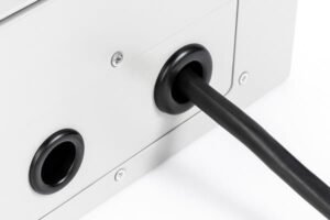 Rubber wire grommet in metal panel hole, securing and protecting power cable entry, used in electrical enclosures or control boxes.