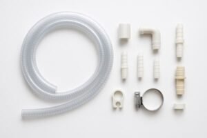 Condensate drain hose kit, transparent braided PVC hose with assorted plastic fittings, elbows, hose clamp, and wall clip, arranged on white background.