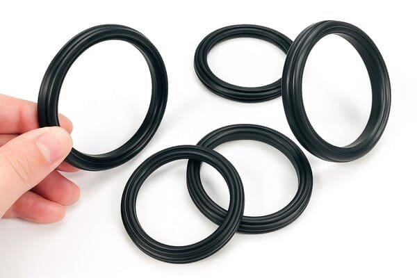 Hand holding black quad ring seal with four additional seals on white background, highlighting multiple sizes for industrial sealing applications.