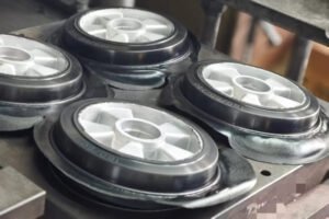 Rubber wheel overmolding, compression mold forming four hubbed wheels, excess flash visible, vulcanization in progress on press.