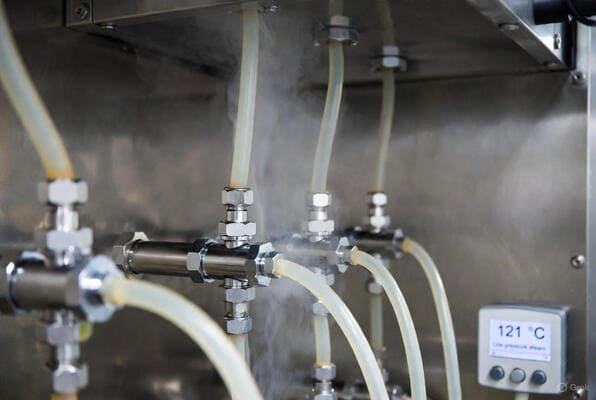Food grade silicone tubes in stainless steam sterilization rig, translucent hoses carrying low pressure steam at 121 °C.