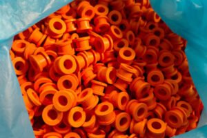 Orange silicone rubber grommets, bulk flanged molded sleeves in a blue bag liner, ready for packing and shipment.