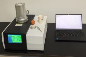 TGA analyzer for rubber compounds, benchtop instrument heating sample crucible while laptop shows weight loss curve in real time.