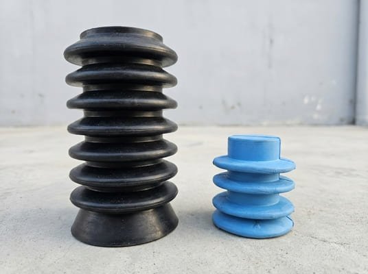 Rubber end cap and bellows, blue protective cap beside black ribbed rubber sleeve, white studio background.