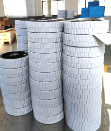 Floor scrubber wheels 200mm, stacked in warehouse, white non-marking tread with ribbed pattern, designed for cleaning machines on smooth floors.